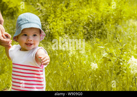 Baby 11 Monate lächelnd zeigt Zähne und die Hand nach vorn ziehen. Kleines Mädchen auf einem Spaziergang in der Natur Stockfoto