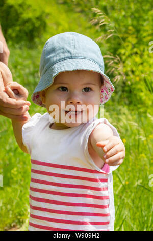 Kleines Mädchen geht mit der Hand in die Kamera. Ein Kind geht auf einer blühenden Wiese, vertikale Portrait. Sonnigen Sommer Porträt eines hübschen Lächeln g Stockfoto