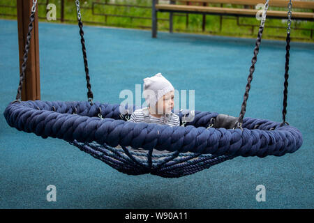 Kleines Baby auf Spinnennetz nest Schwingen. Baby Boy 1 Jahr Schwingen auf einer Schaukel im Garten Stockfoto