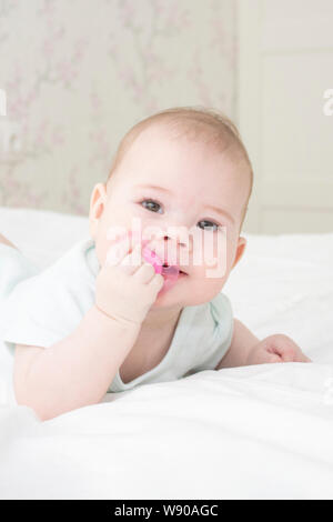 Baby girl portrait Close-up Vertikale. Das Gesicht des Babys ist 6 Monate alt, auf dem Bauch liegend in weißen Kleidern, und zieht die Brustwarze in den Mund, weiche fo Stockfoto