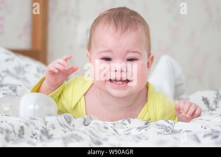 Baby 6-7 Monate weinen liegen auf dem Bauch. Kaukasische junge Mädchen Kind Kleinkind Säugling in gelb Schreie und zeigt 2 Baby Zähne, Zahnen, Porträt, so Stockfoto
