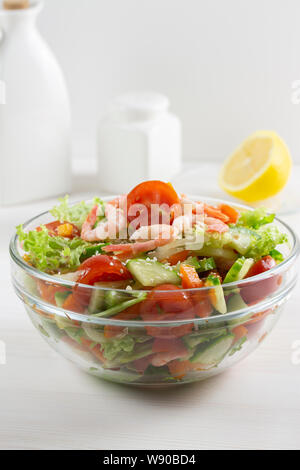 Salat von frischem Gemüse und Meeresfrüchte Tomaten Gurken Grüns Sesam Garnelen in einem durchsichtigen Glas Schüssel auf einem hellen Hintergrund. Vegan Vegetarisch foo Stockfoto