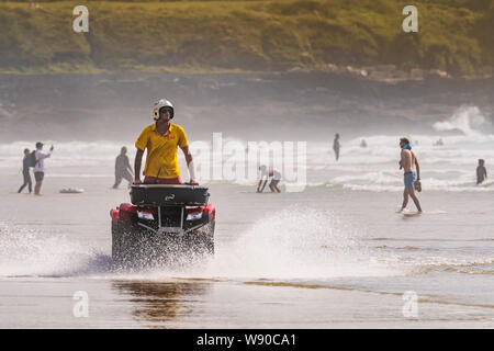 Ein rnli Rettungsschwimmer reiten ein Quad und patrouillieren entlang der Küstenlinie an Fistral Beach in Newquay in Cornwall. Stockfoto