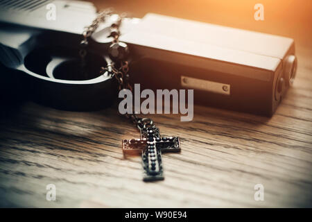 Auf einem Tisch liegt ein Gewehr durch Sonnenlicht beleuchtet und Schwarz geschnitzten Heiligen Kreuz mit schwarzen Perlen auf der Kette. Stockfoto