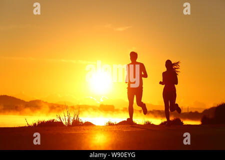 Zurück licht Portrait von ein paar shilouette von Läufern bei Sonnenaufgang am Strand Stockfoto