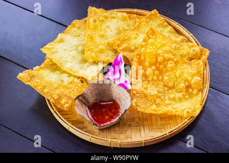 Gelbe gebratene Knödel und eine Tasse Soße auf einer Bambus Teller mit Orchideen auf dem Tisch platziert aus dunklem Holz eingerichtet. Stockfoto