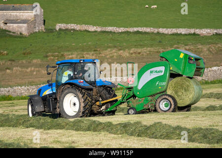 Die heulage Erntegut auf der Alm mit einem New Holland T6030 und ein McHale 5500 Ballenpresse. Cumbria, Großbritannien. Stockfoto