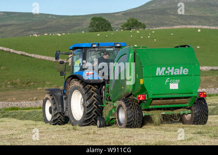 Die heulage Erntegut auf der Alm mit einem New Holland T6030 und ein McHale 5500 Ballenpresse. Cumbria, Großbritannien. Stockfoto