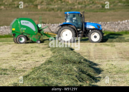 Die heulage Erntegut auf der Alm mit einem New Holland T6030 und ein McHale 5500 Ballenpresse. Cumbria, Großbritannien. Stockfoto