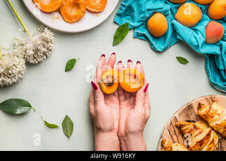 Weibliche Hand halbiert Apricot mit Kernel auf leichte Küche, Schreibtisch mit Croissants und zerstreut, Aprikosen, Ansicht von oben Stockfoto