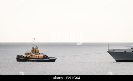 Ein Schubschiff unterstützt die SAS AMATOLA von Simons Town Flottenstützpunkt auf Südafrika der False Bay Küste in der Nähe von Kapstadt Stockfoto