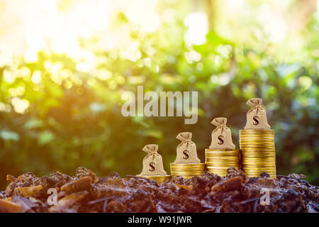 Geld verdienen und Geld Investitionen Konzept. Eine Geld-Beutel auf sich Stapel von Münzen auf die gute Erde und Natur Hintergrund mit Sonnenlicht. Zeigt langfristige Stockfoto