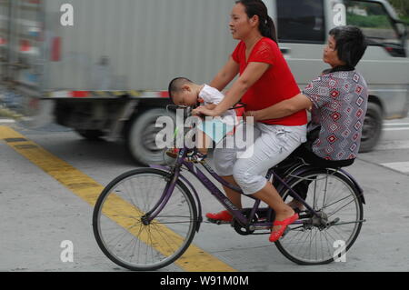 ---- Eine weibliche Chinesische Wanderarbeiter reitet ein Fahrrad ihren Kindern und der Mutter, die auf einer Straße in ChangAn town Dongguan City, South China Guangd Stockfoto