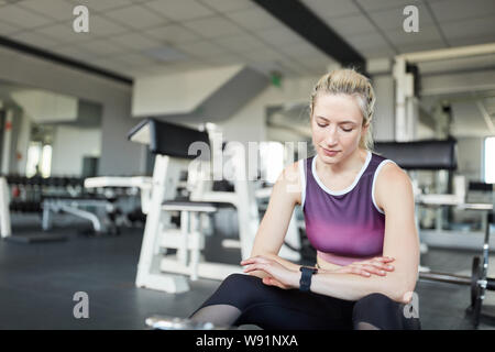 Junge Frau steuert Fitness mit smartwatch in einer Pause im Fitnesscenter Stockfoto