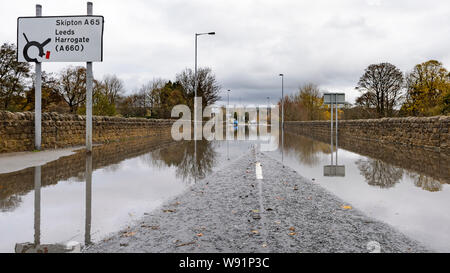 Überschwemmung - Überflutete Straße (autofrei) mit Bäumen & Zeichen in ständigen Hochwasser - Burley in Bösingen, Yorkshire, England, UK wider. Stockfoto