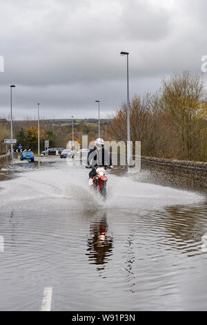 Überschwemmung - motorradfahrer Reiten (Spritzwasser) Motorrad in Hochwasser auf überschwemmten Straßen, unpassierbare zu Autos - Burley in Bösingen, Yorkshire, England, Großbritannien Stockfoto