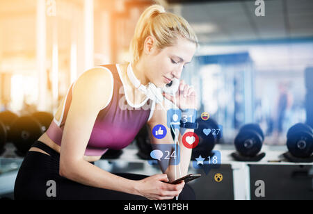 Junge Frau gibt Bewertung auf dem Smartphone beim Trainieren im Fitnesscenter Stockfoto