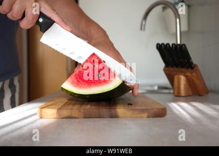 Nahaufnahme der Frau Hand schneiden Wassermelone auf Holz Schneidebrett in der Küche Stockfoto