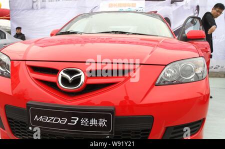 ---- Ein Mann schließt die Tür eines Mazda3 auf dem Display während ein Auto Show im xuchang Stadt, zentrale China Provinz Henan, 29. März 2013. Eine Wiederherstellung Stockfoto