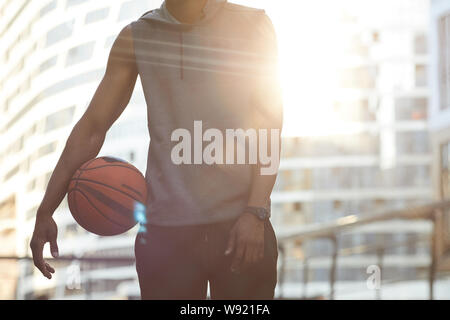 Im mittleren Abschnitt Portrait von Stattlichen afrikanischen Mann mit Ball beim Stehen in der basketballplatz durch Sonnenlicht beleuchtet, kopieren Raum Stockfoto