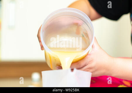 Schuß von SOAP-Mix, Backmischung, Ghee aus einem kunststoffbecher in ein anderes geopfert, hausgemachte Seife zu machen. Diese Mischung aus Ölen wie Kokosnuss-, Oliven Stockfoto