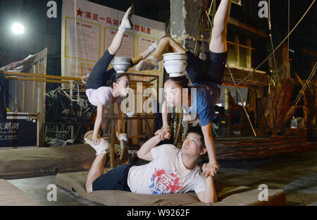 Eine junge chinesische Acrobat unterstützt zwei junge Mädchen, wie sie ihre Körper und Balance Schüsseln auf dem Kopf im Ausbildungszentrum des Soldaten Acro Bend Stockfoto