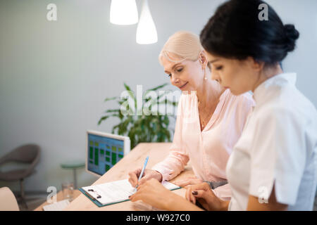 Frau die Unterzeichnung eines Vertrags mit ihrem Zahnarzt. Stockfoto