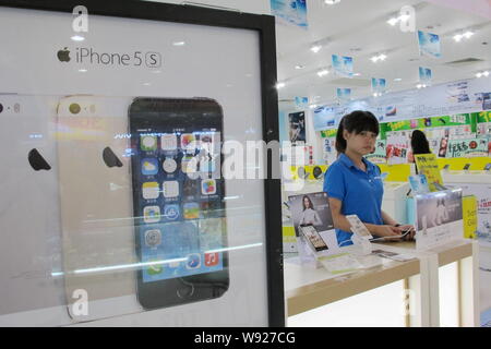 ---- Ein Mitarbeiter gesehen wird, neben einer Werbung für iPhone 5s Smartphones von Apple zu einem Handy store in Haikou, South China Hainan provinc Stockfoto