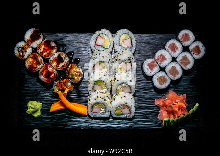 Eine Auswahl der verschiedenen Arten von Sushi Rollen auf eine schwarze Keramikplatte garniert mit Ingwer und Wasabi vorgestellt Stockfoto