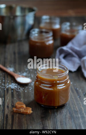 Kleine Gläser gesalzen Karamell Sauce über eine rustikale Tabelle. Selektiver Fokus mit unscharfem Hintergrund. Stockfoto