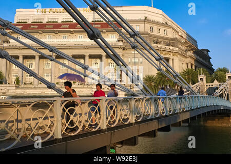 Touristen über die cavenagh Brücke überspannt den Fluss Singapur, Singapur, die ikonische Fullerton Hotel, die ehemalige G.P.O. Gebäude im Hintergrund Stockfoto