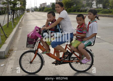 ---- Eine weibliche Chinesische Wanderarbeiter reitet ein Fahrrad ihre Kinder nehmen in Dongguan City zur Schule, South China Guangdong Provinz, 22. Juni 2010 Stockfoto