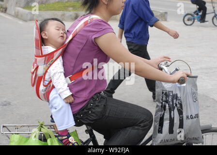 ---- Eine weibliche Chinesische Wanderarbeiter ihrem schlafenden Baby auf dem Rücken reitet auf einer Straße in ChangAn town Dongguan City, South China Guangdon Stockfoto