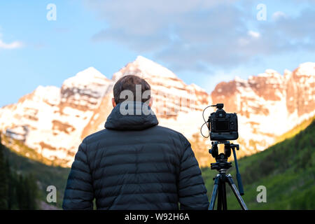 Kastanienbraune Glocken bei Sonnenaufgang mit Rückseite des Menschen Fotograf und Stativ in Aspen, Colorado mit Rocky Mountain Peak und Schnee Stockfoto