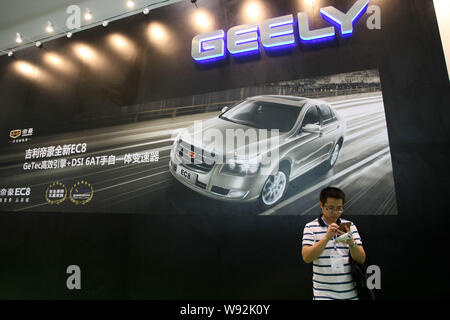 ---- Ein Besucher schaut auf sein Handy vor dem Stand von Geely während einer Ausstellung in Shanghai, China, 4. Juni 2013. Chinesischen Automobilhersteller Geely Aut Stockfoto