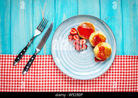 Russische syrniki oder Quark Krapfen oder Pfannkuchen mit Erdbeeren auf Blau Holz Hintergrund serviert. Ansicht von oben Stockfoto