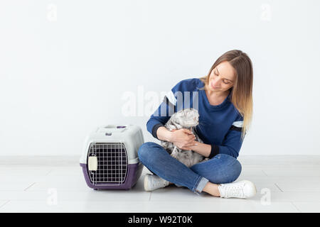 Charmante positive junge Frau hält in ihrer Hände ihre schönen grauen schottischen Katze sitzt auf dem Boden in eine neue Wohnung. Pet-Konzept. Stockfoto