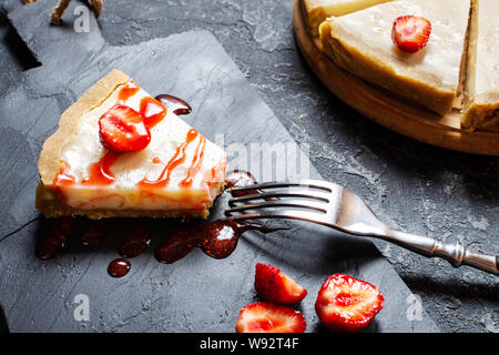 Scheibe hausgemachten Käsekuchen mit frischen Erdbeeren auf schwarzen Stein Hintergrund Stockfoto