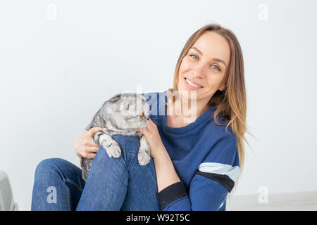 Charmante positive junge Frau hält in ihrer Hände ihre schönen grauen schottischen Katze sitzt auf dem Boden in eine neue Wohnung. Pet-Konzept. Stockfoto