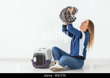 Charmante positive junge Frau hält in ihrer Hände ihre schönen grauen schottischen Katze sitzt auf dem Boden in eine neue Wohnung. Pet-Konzept. Stockfoto