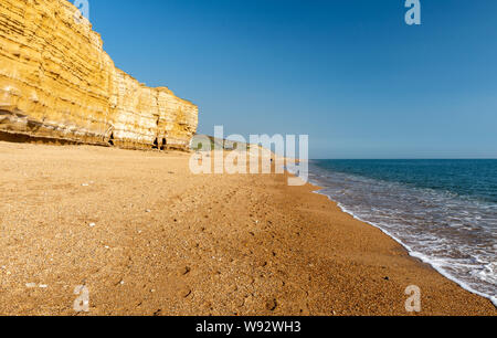 Sonne scheint auf den Schindel der Hive Strand, Teil der Chesil Beach, unter der Sandsteinfelsen von Burton Bradstock auf in Dorset Jurassic Coast. Stockfoto