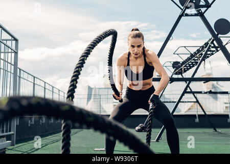 Frau in Fitness Tragen Sie arbeiten mit zwei Schlacht Seile auf der Dachterrasse Stockfoto