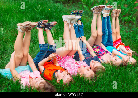Kinder liegen auf grünen Gras im Park im Sommer mit ihren Beinen hob in den Himmel. Stockfoto