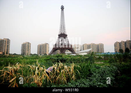 Ein chinesischer Bauer bewässert sein Feld in der Nähe der Hälfte - sortierte Kopie des Eiffelturms an Tianducheng, eine kleine chinesische Gemeinschaft Paris repliziert, in Hangzhou Stockfoto