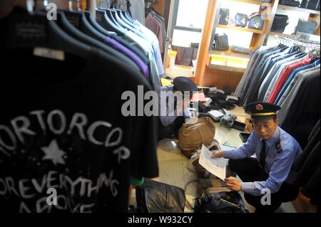 Chinesische Polizeibeamte fake Luxus Marke T-Shirts und Handtaschen in einem Geschäft in Peking, China konfiszieren, 13. Mai 2013. Beijing Polizei und l Stockfoto