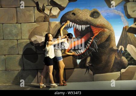 Chinesische Besucher stellen ihre Hände in ein Dinosaurier Mund für eine 3D-Aufnahme während der lebendig Trick, Kunst, 3-D-Ausstellung in Shenyang, China, 6. August Stockfoto