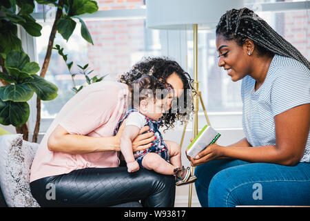 Seitenansicht der lächelnden Mütter zeigt Bild Buch zu süßen Sohn, während zu Hause sitzen Stockfoto
