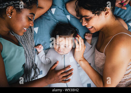 Ansicht von oben der glücklichen Freundinnen mit niedlichen schlafenden Baby Boy ruht auf Bett Stockfoto