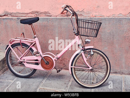 Altes rotes Fahrrad mit Korb, der an die alte Mauer an der Ziegelsteinstraße gelehnt ist Stockfoto