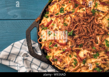 In der Nähe von bayrischen Spätzle mit Käse und Speck in einem Guss Fach, auf einer blauen Tabelle. Oben Ansicht der Deutschen traditionellen Mahlzeit. Flach von Ch Stockfoto